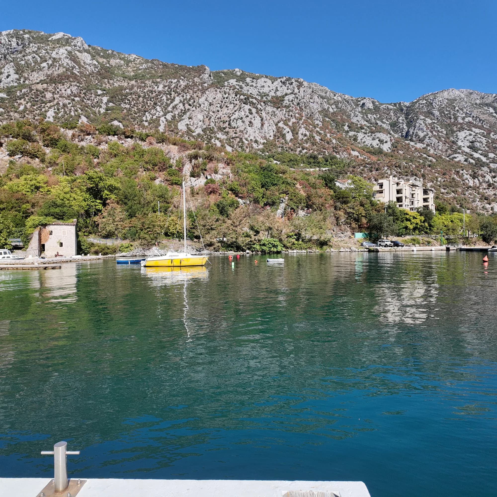 Stone houses and moored boats at the mouth of the Morinj cove, the karst slope rising behind