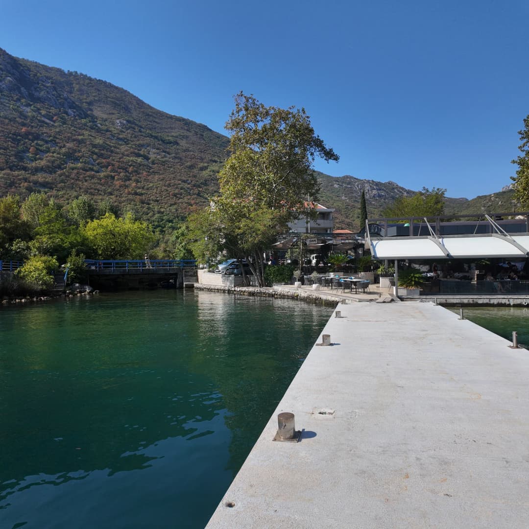 The jetty at Morinj over clear green water, the restaurant pavilion under the plane trees