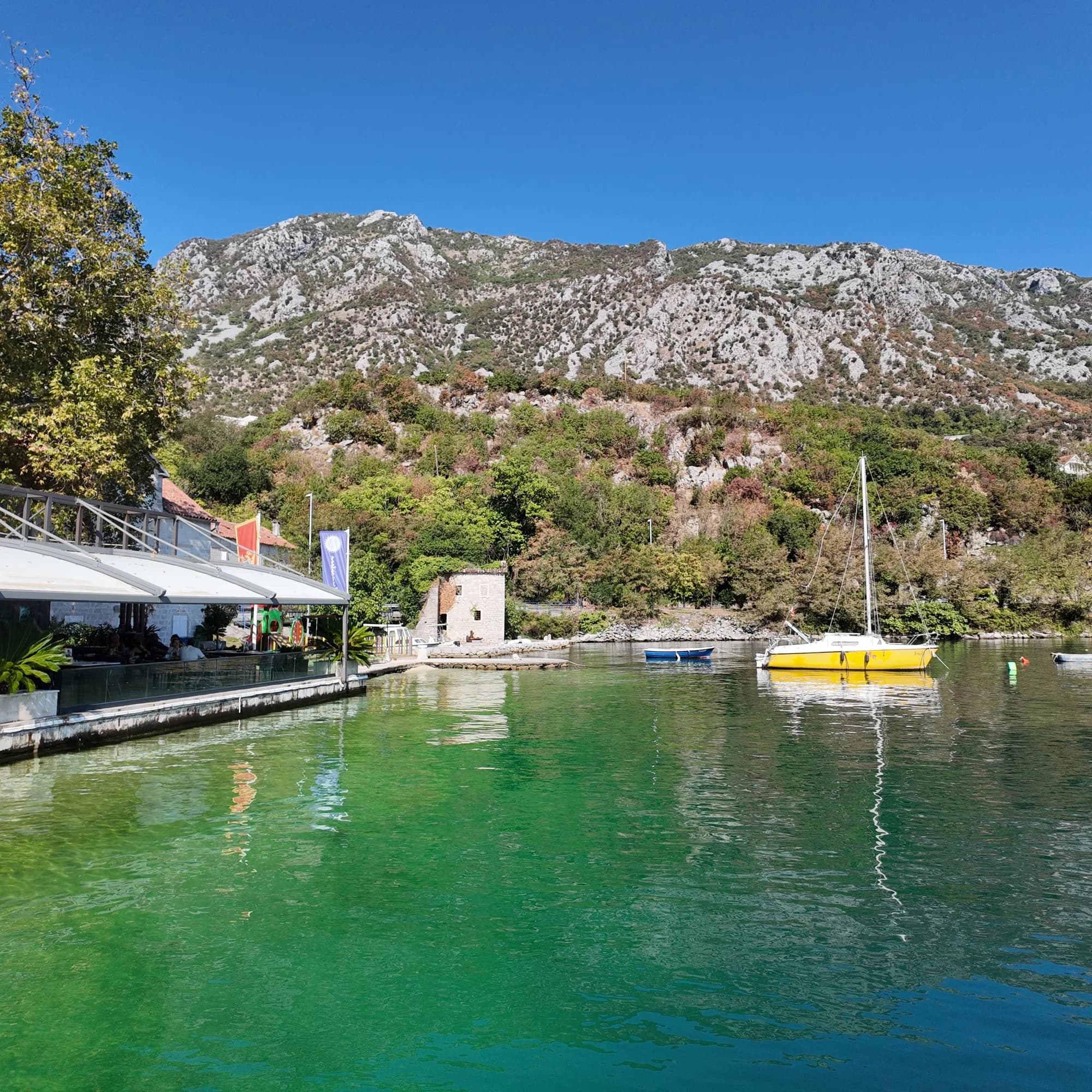 The green millstream cove at Morinj with the restaurant pavilion on the left, a yellow sailing boat moored below the old stone mill