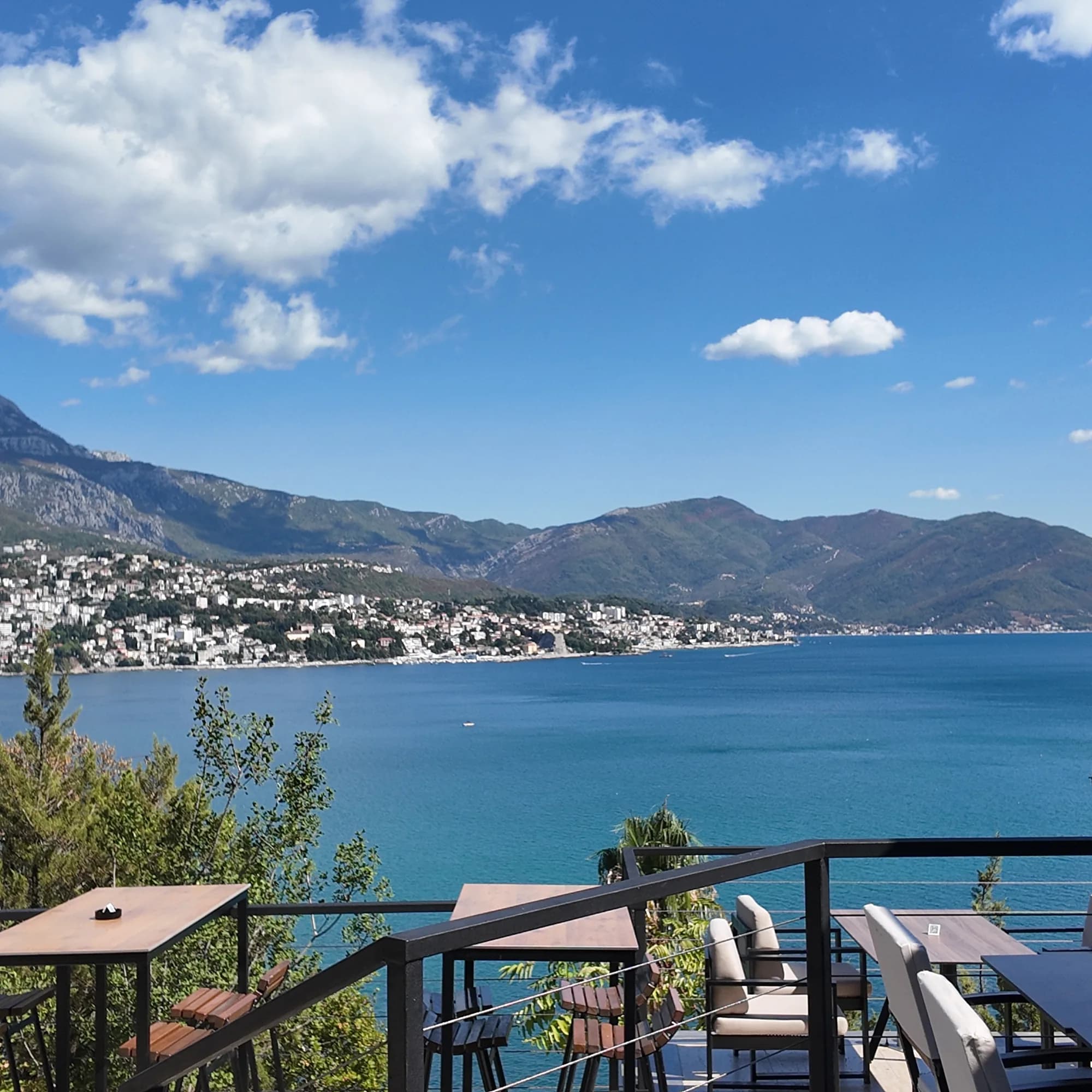 A café terrace above the water at Njivice, the whole Herceg Novi riviera across the bay