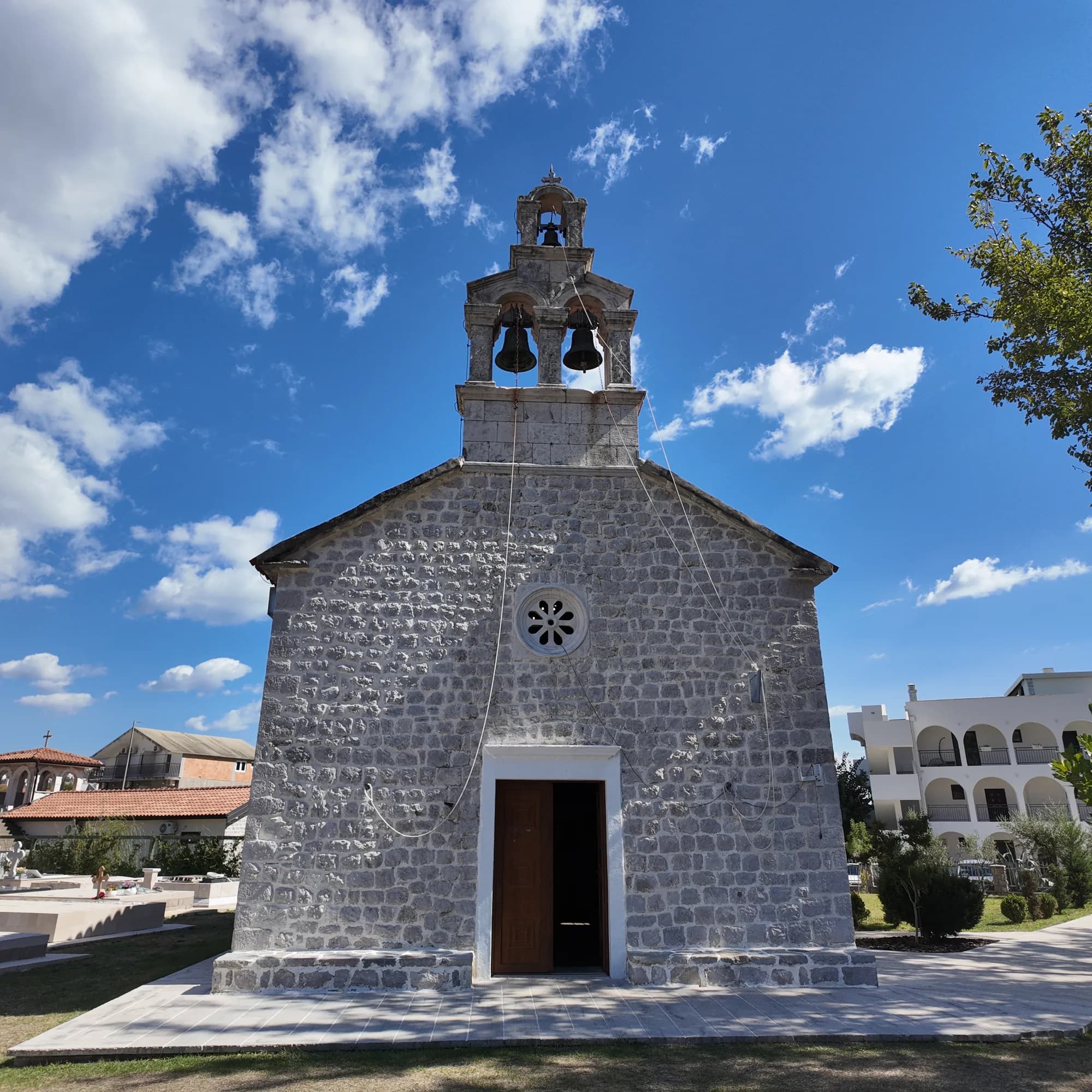 The church of the Transfiguration at Sutorina, between Njivice and Igalo — built in 1832, razed in 1857, rebuilt by 1875 — with its three-bell belfry and the village cemetery
