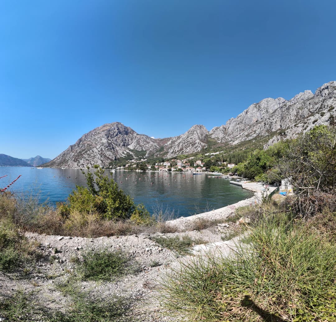 The curve of the Orahovac shore, gravel and scrub at the water’s edge