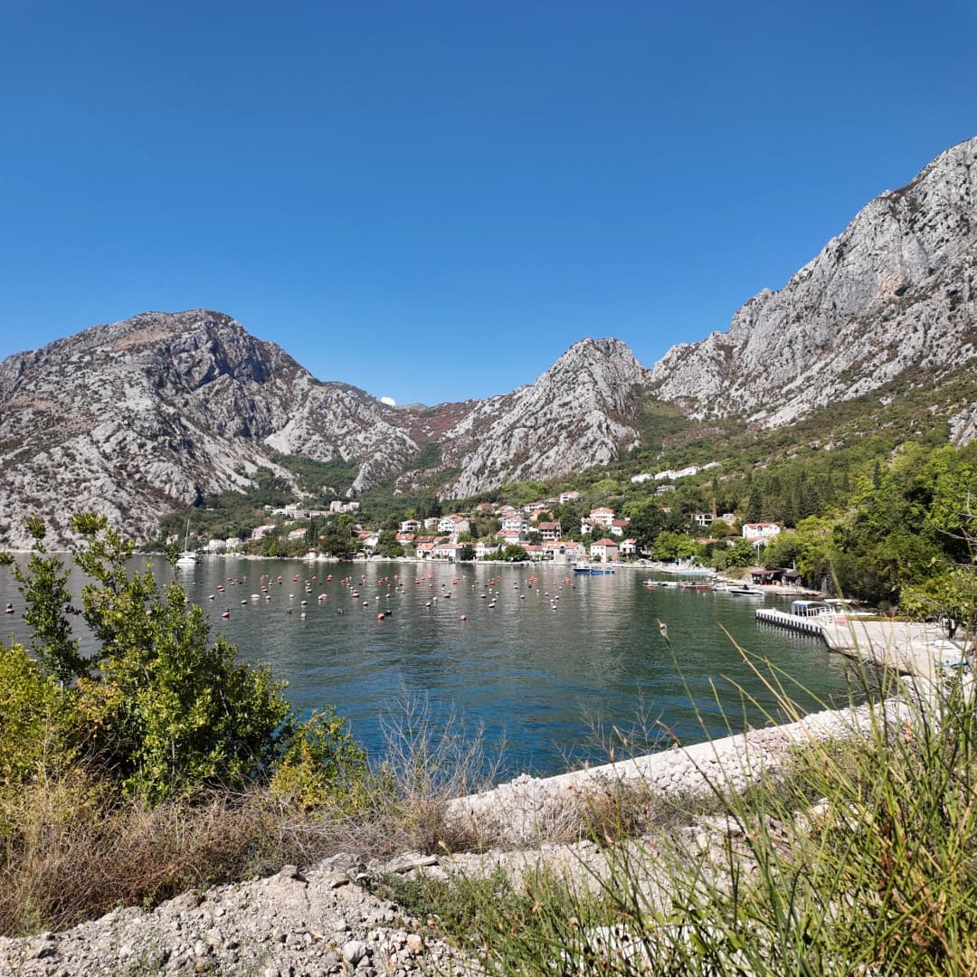 Orahovac’s houses along the shore under the bare limestone wall, the inner Bay of Kotor flat in September sun