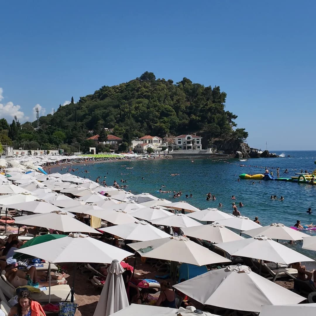 Rows of umbrellas on Petrovac beach with a headland closing the far end.