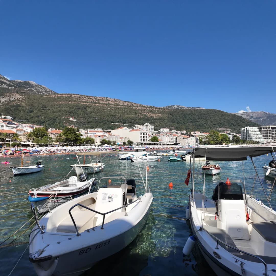 Small boats moored in Petrovac harbour with a mountain ridge rising behind.