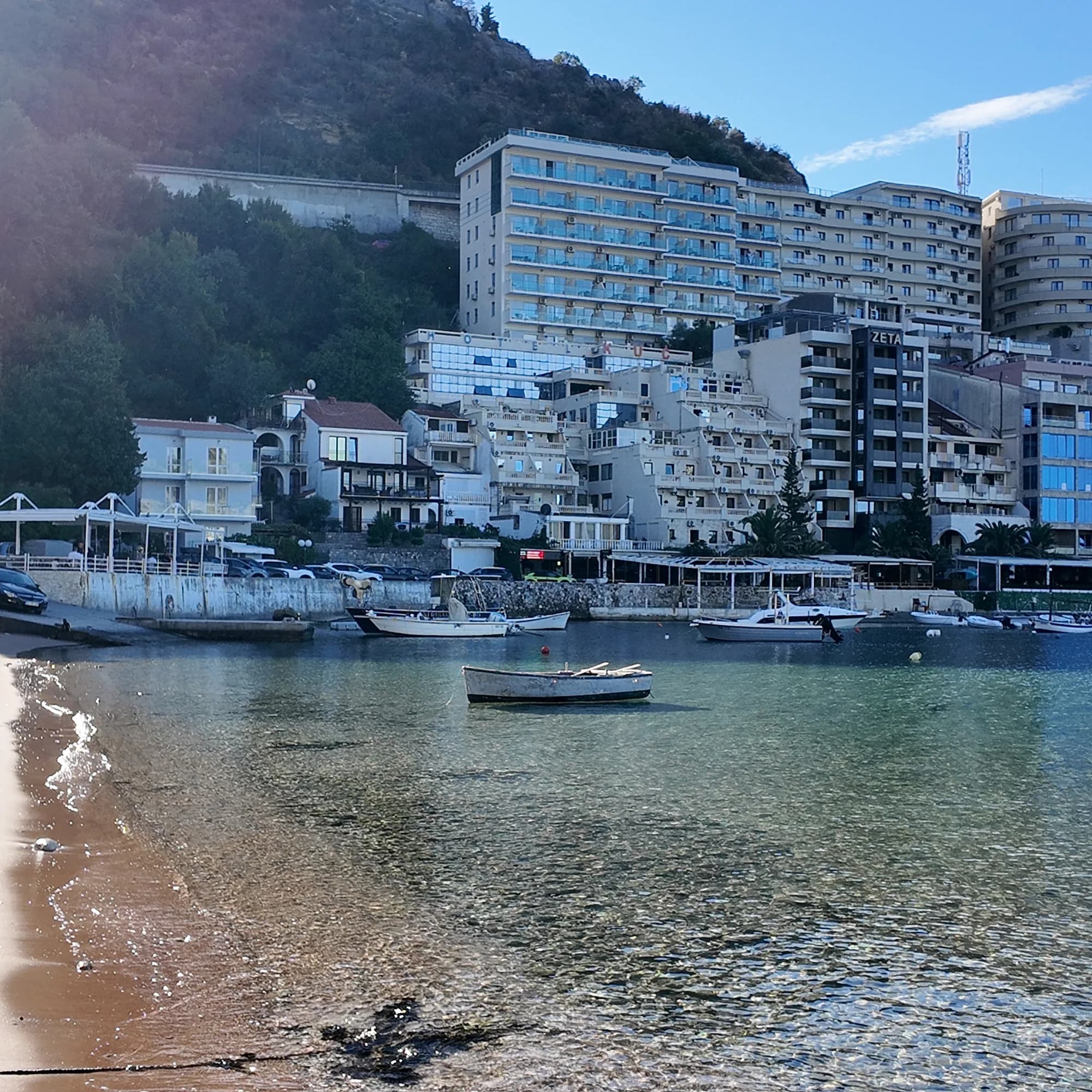 The Rafailovići mooring on a clear morning: boats behind the breakwater, the apartment blocks and the hills in full sun