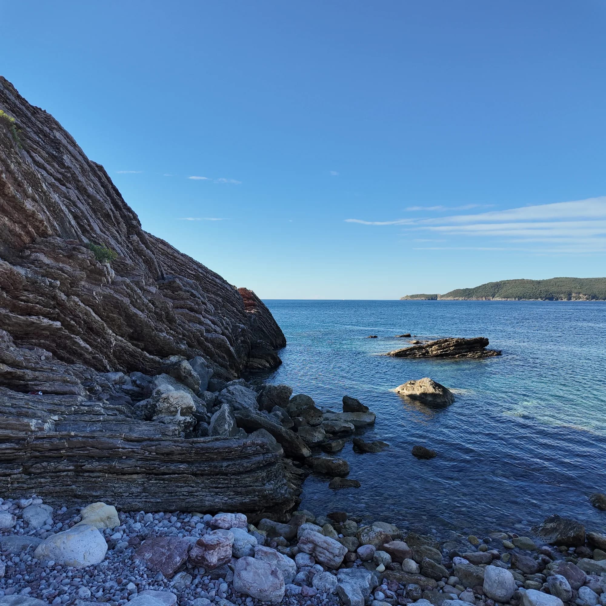 The striated rock of Cape Đevištenje in morning light, the sea flat and blue and Sveti Nikola island on the horizon