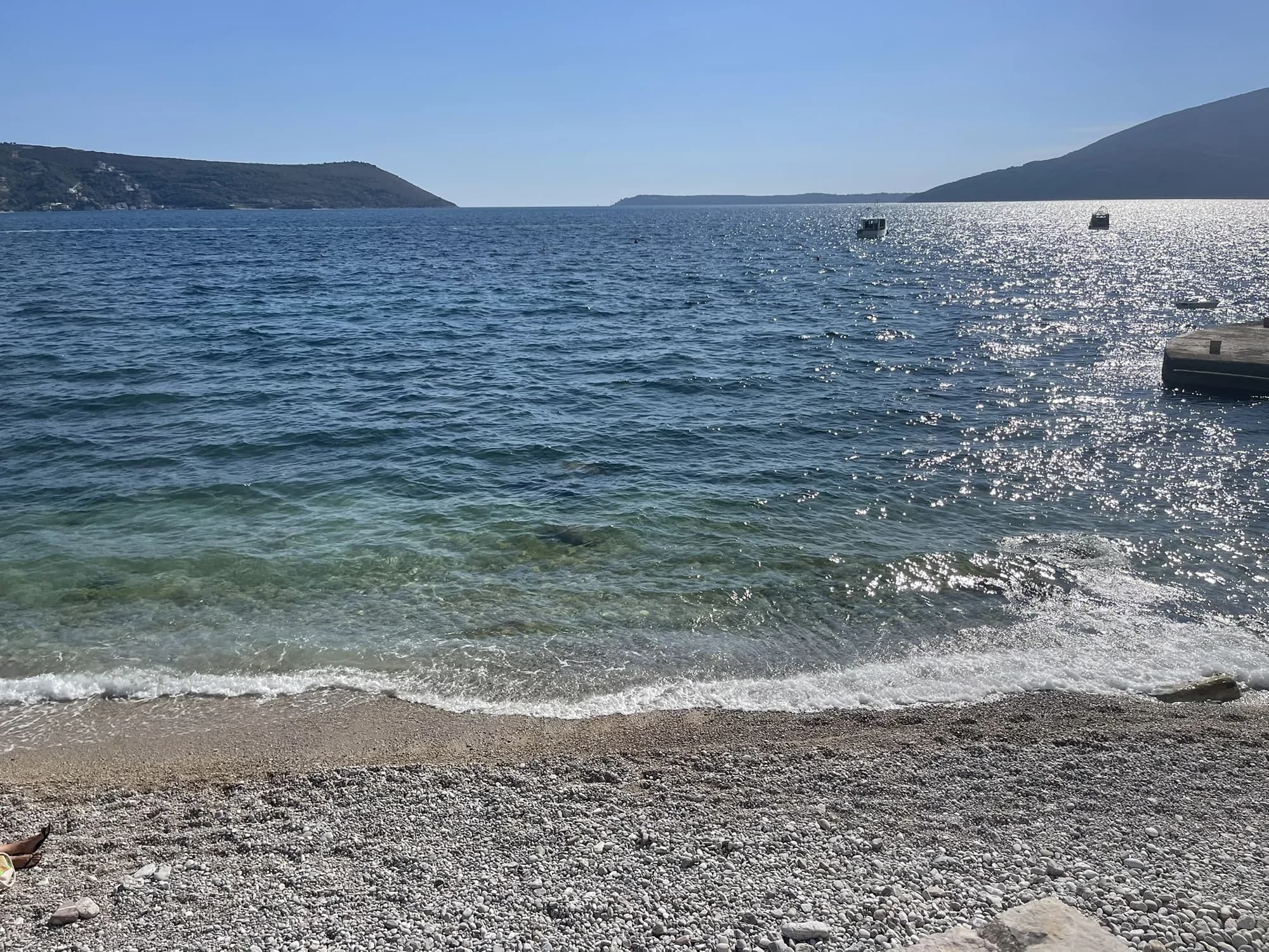 The pebble shore and clear water at Ćorovića beach in Savina, looking through the mouth of the Bay of Kotor