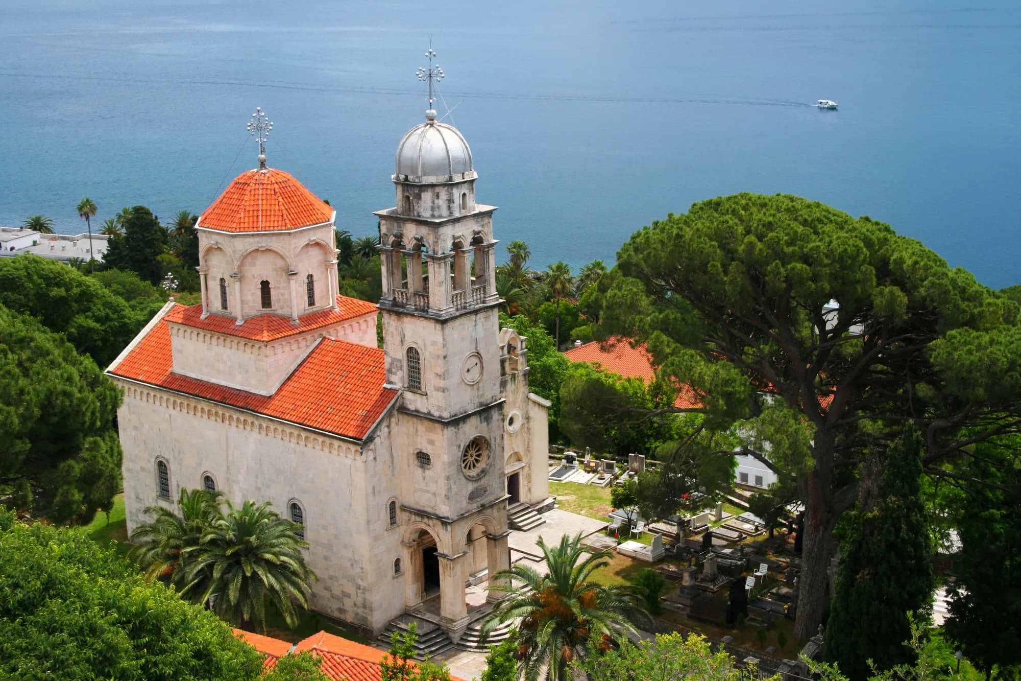 Savina monastery from the hill above: the church, its cemetery and roofs among umbrella pines, the open water of the bay beyond
