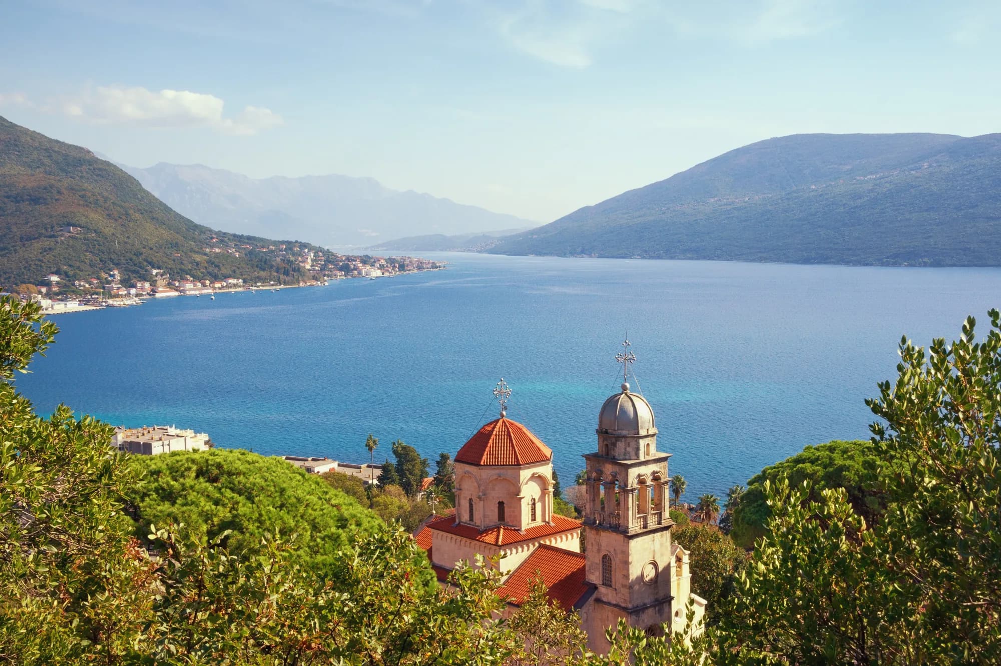 The monastery church half-hidden in greenery on the shoulder above the bay, the strait running out to sea between mountain shores