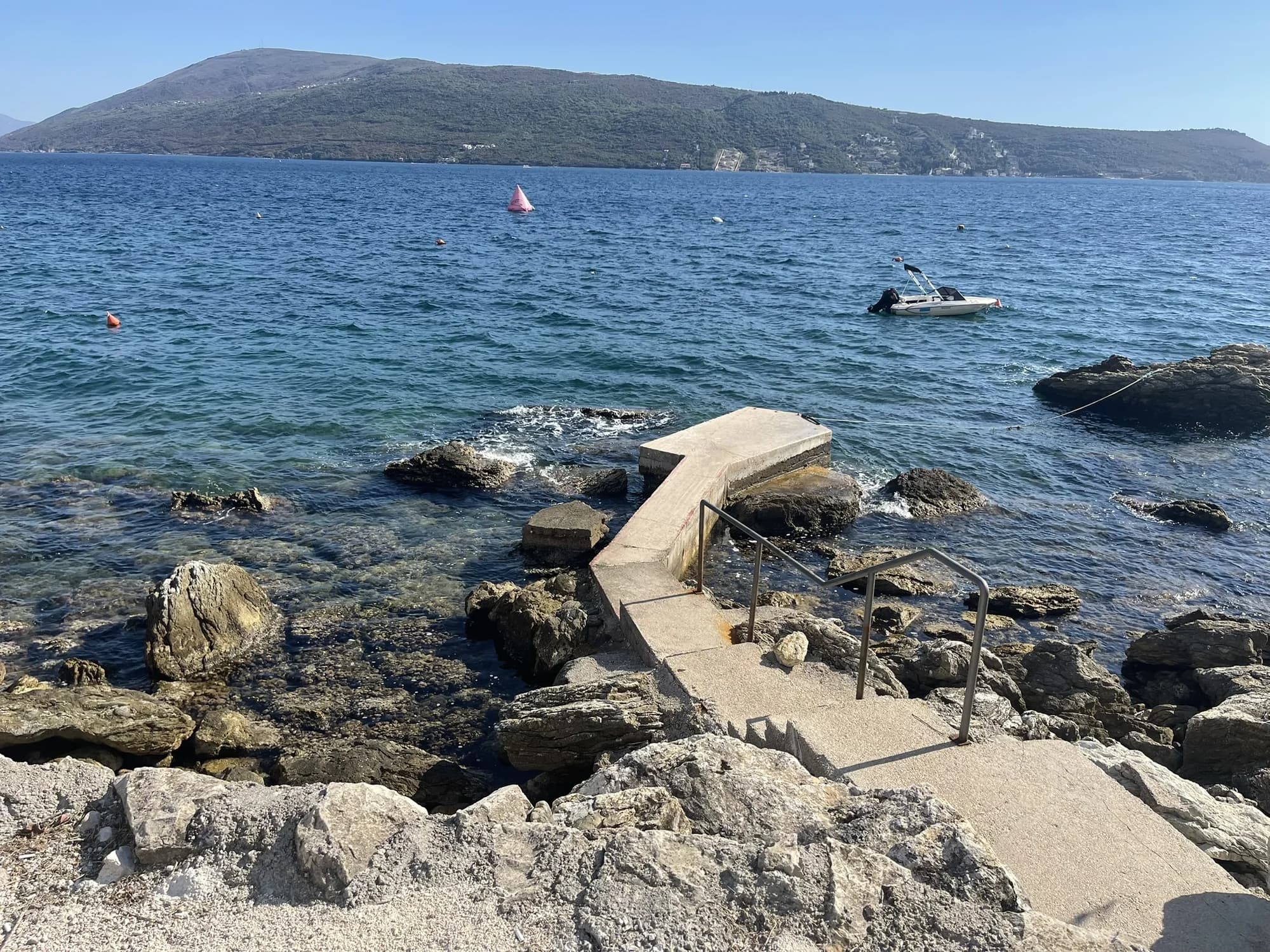 Steps and a narrow concrete platform entering the clear water among rocks at Savina