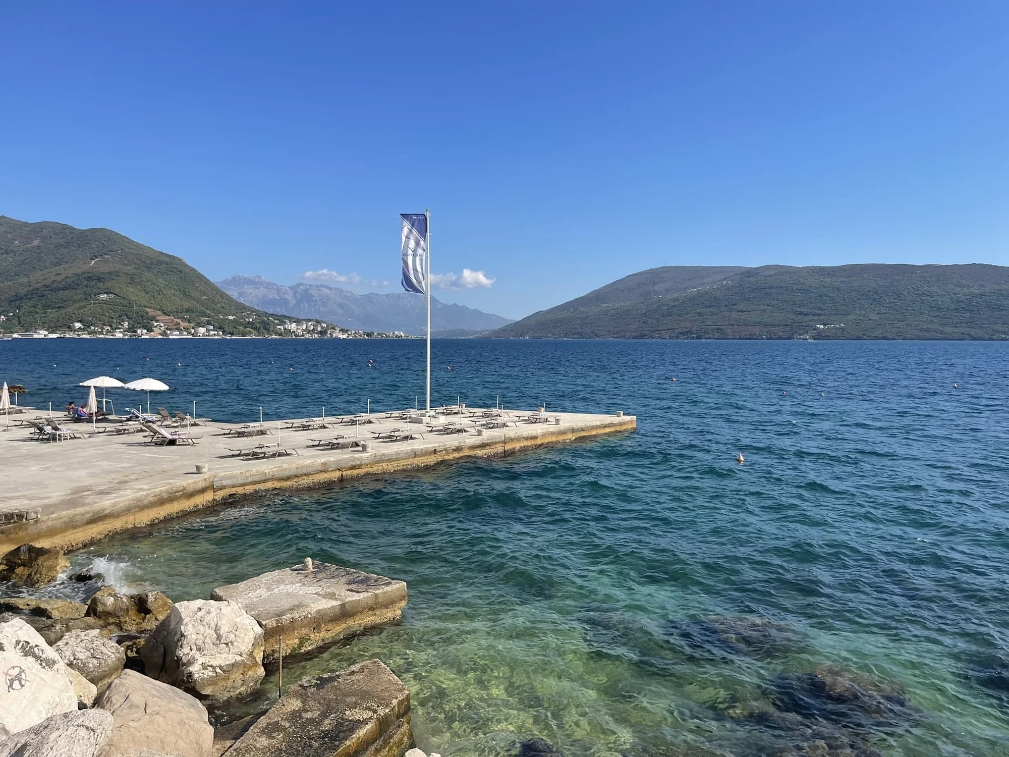 A low stone swimming platform on the Savina waterfront with the Luštica shore across the bay