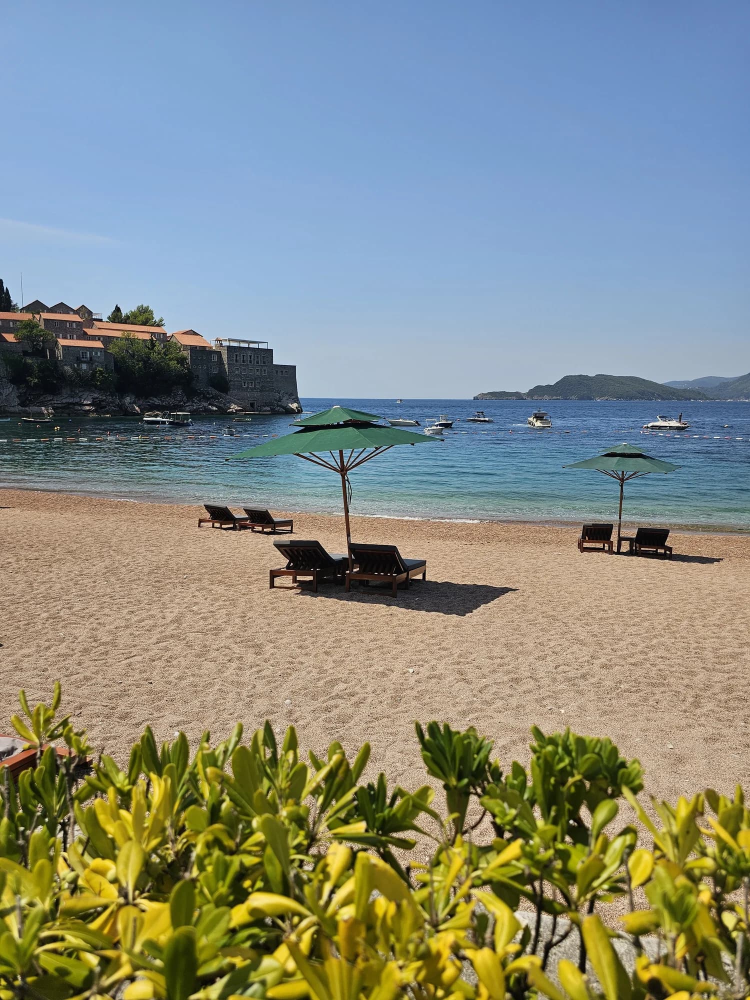 The public northern beach at Sveti Stefan, its green umbrellas, clear shallows and the fortified island