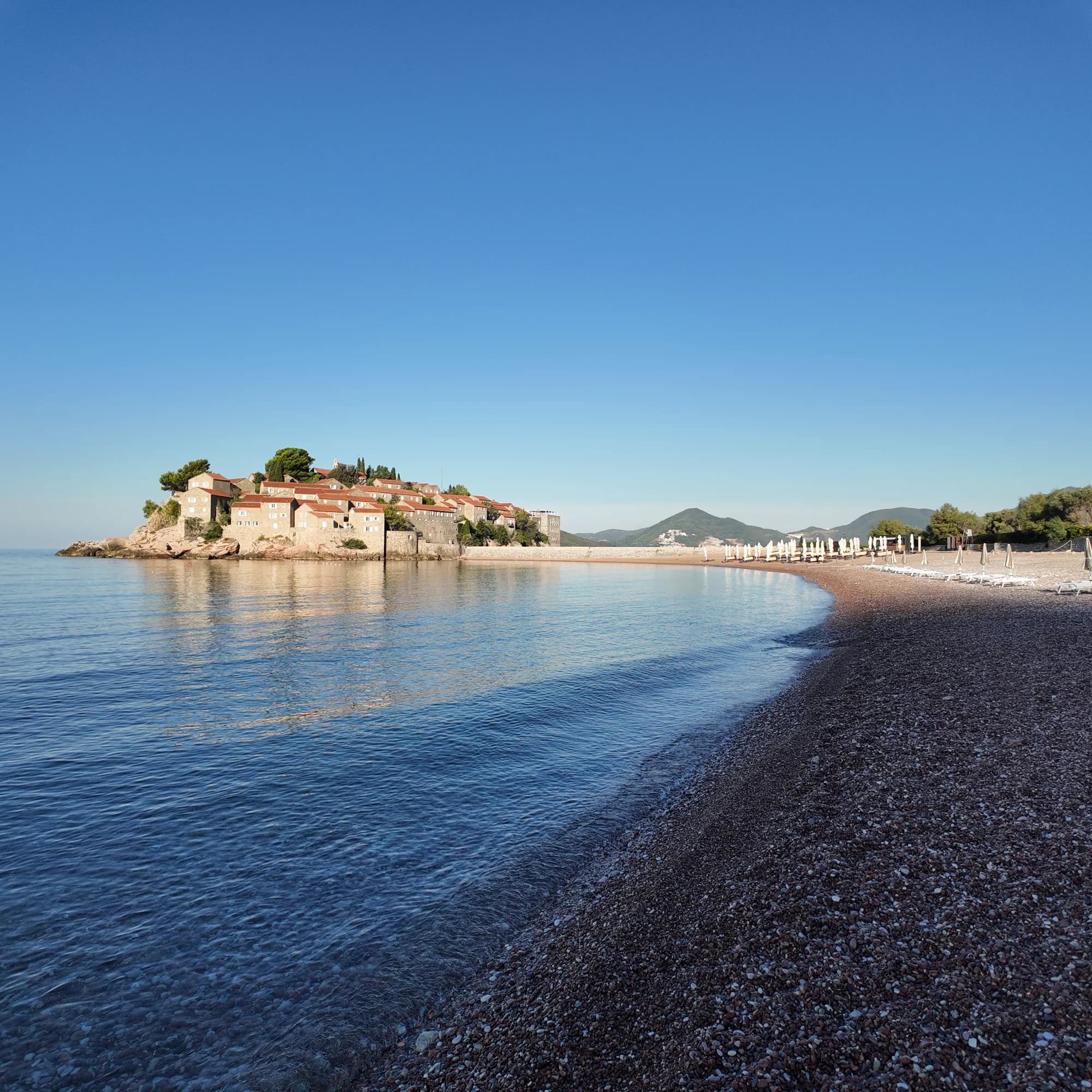 The sunlit north beach curving towards Sveti Stefan across calm morning water