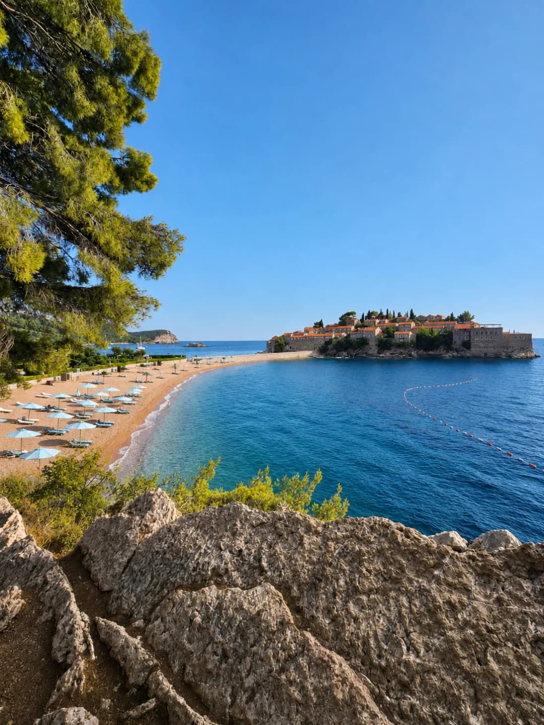 Sveti Stefan island, the causeway and the northern beach seen from the rocky pine path above the bay