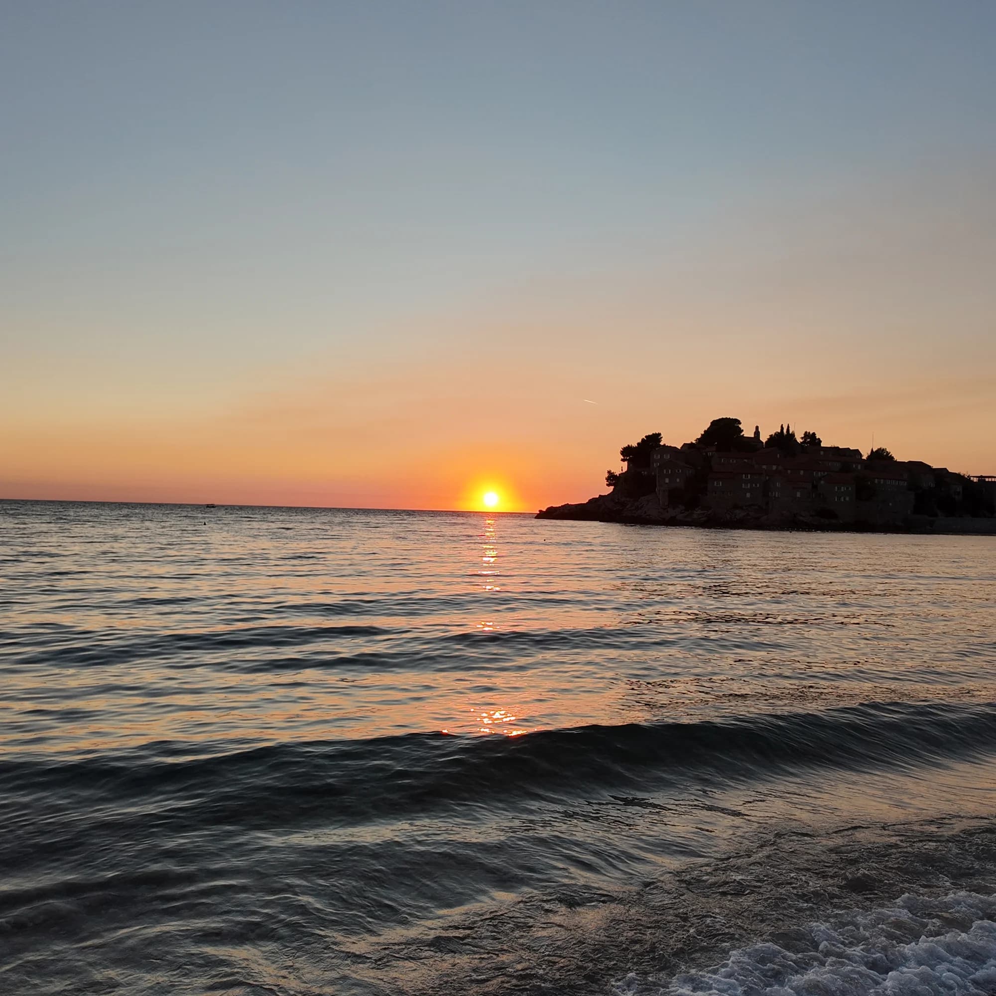 Small evening waves catching the sunset beside the dark outline of Sveti Stefan island