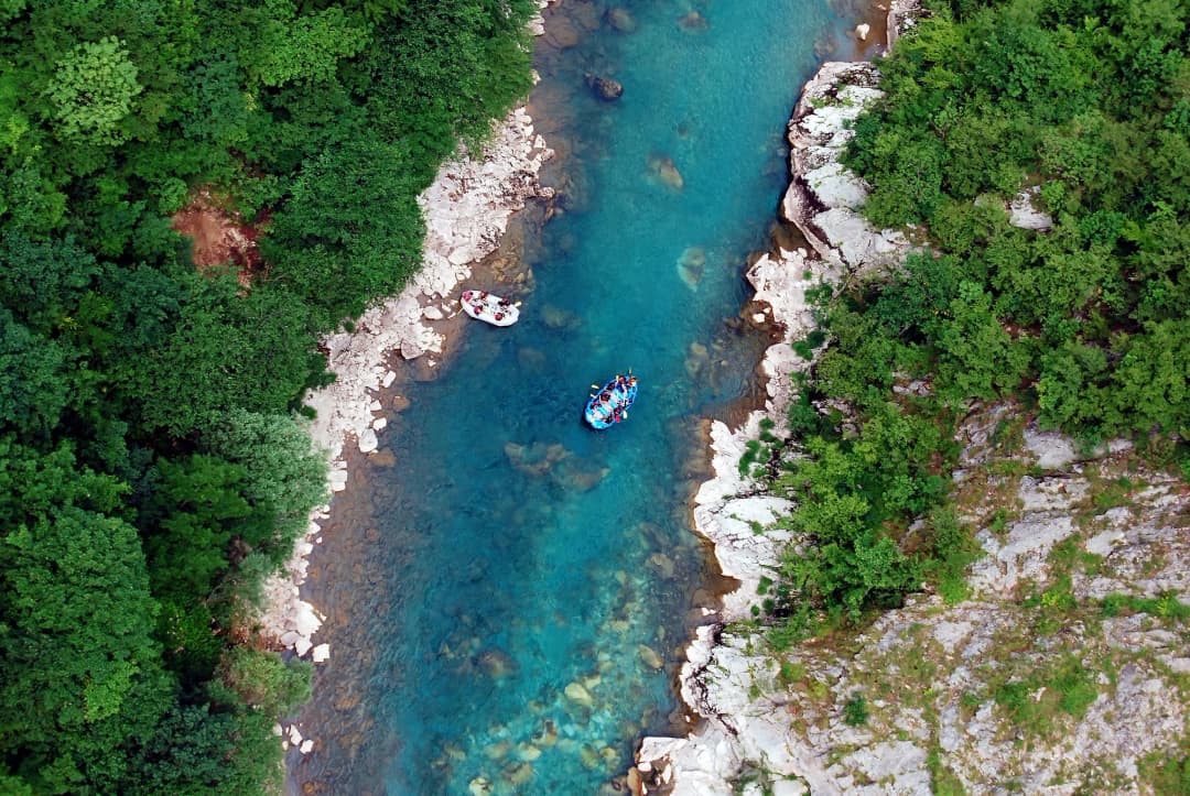 An aerial view of a raft carrying paddlers down a green mountain river between steep forested canyon walls
