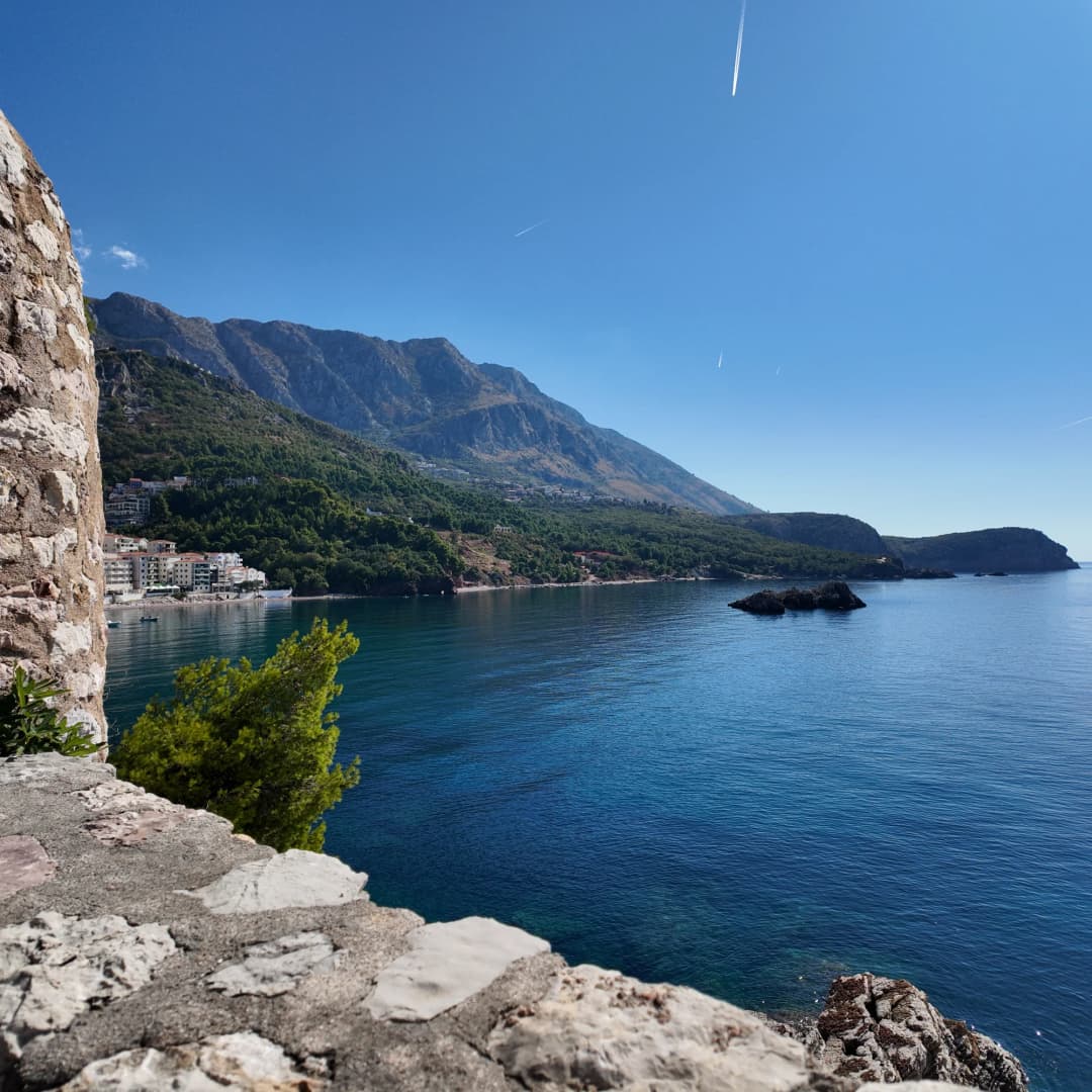 Pogled sa kamenog zida Svetog Stefana preko plave vode na planinsku obalu