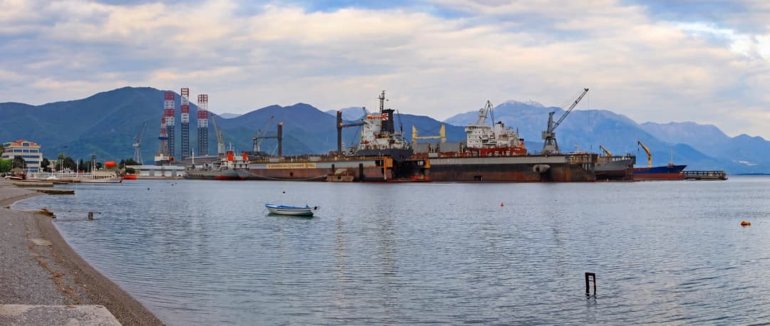 Large yachts moored at the Bijela shipyard, with dock structures and cranes along the repair quay.