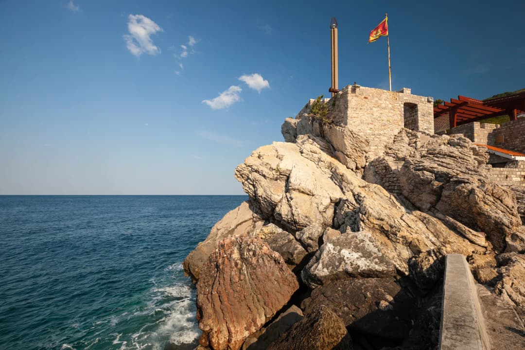 The layered rock base of the Kastello fortress with the Montenegrin flag above