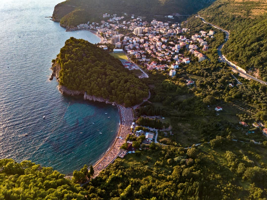 Aerial view of Lučice beach at golden hour with Petrovac behind the pine headland