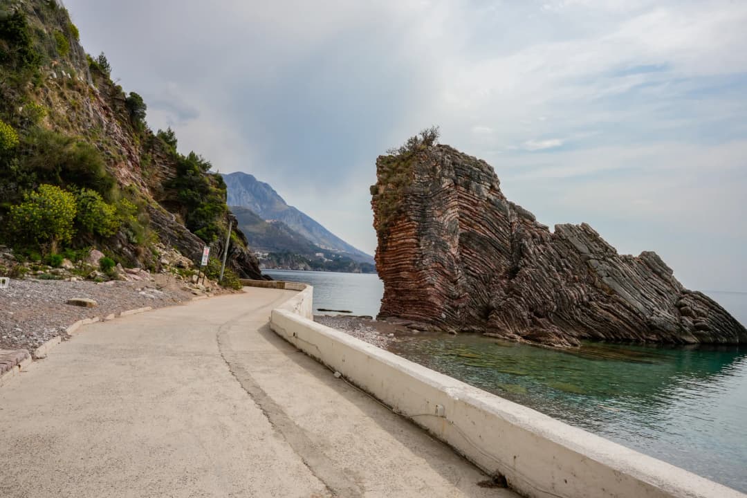 The coastal walking path past a layered red rock formation near Rafailovići