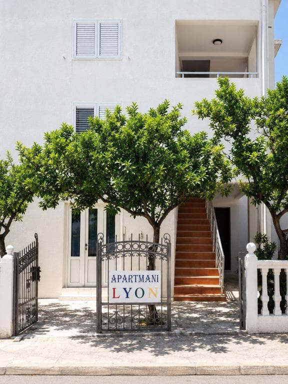 Entrance gate and sign of Lyon Apartmani in Budva, with staircase and citrus trees