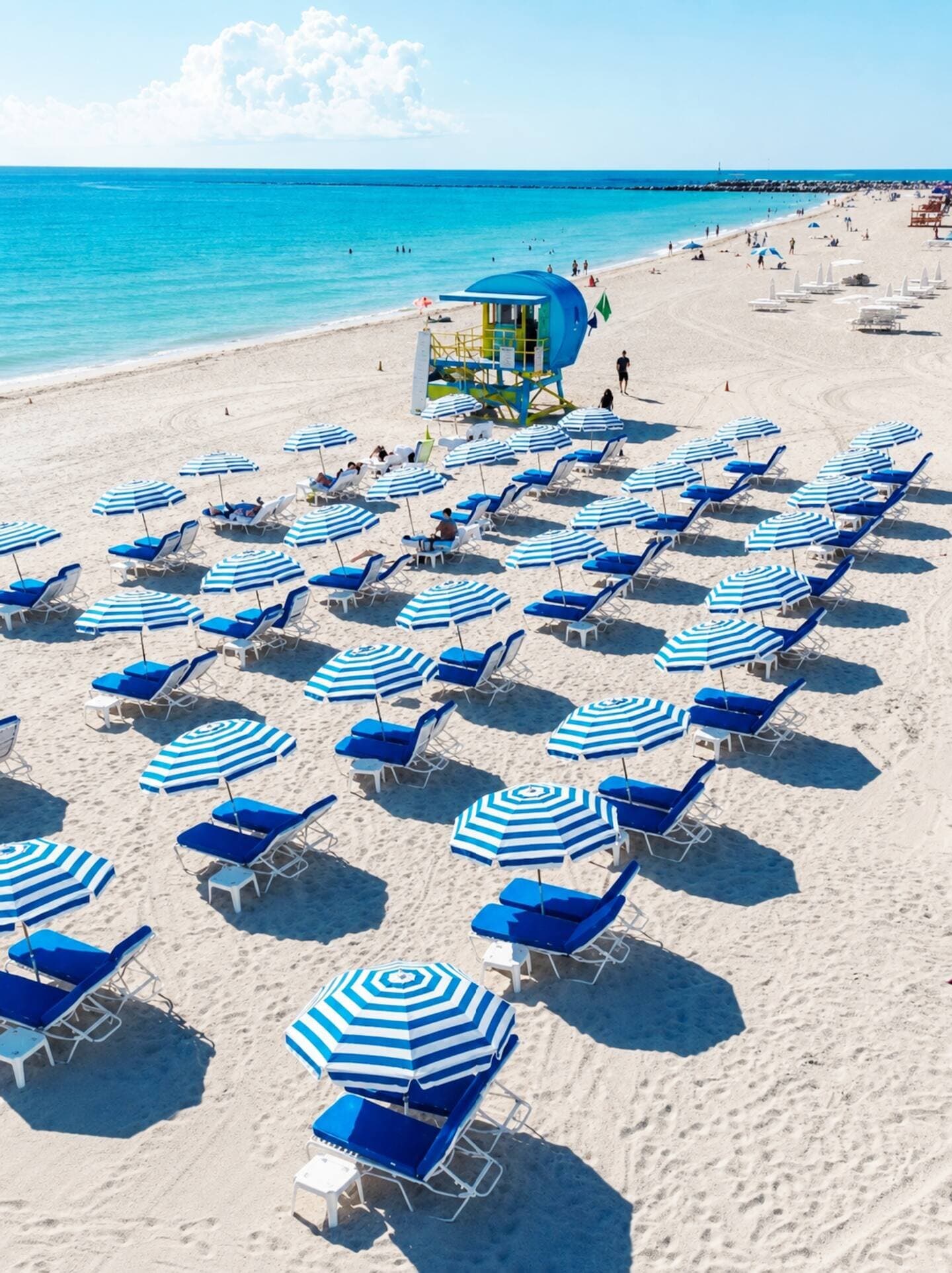 Rows of blue-striped umbrellas and loungers at the Bentley Beach Club, lifeguard tower behind