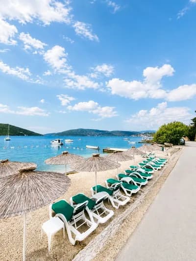 Straw umbrellas and green loungers on the Kumbor beach below the villa