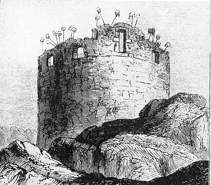 An 1848 engraving of the Tablja: a squat round stone tower standing on bare rock, its parapet ringed with severed heads mounted on spikes, a cross-shaped opening in the upper wall and rectangular openings below, with the tower's top left rough and unfinished.