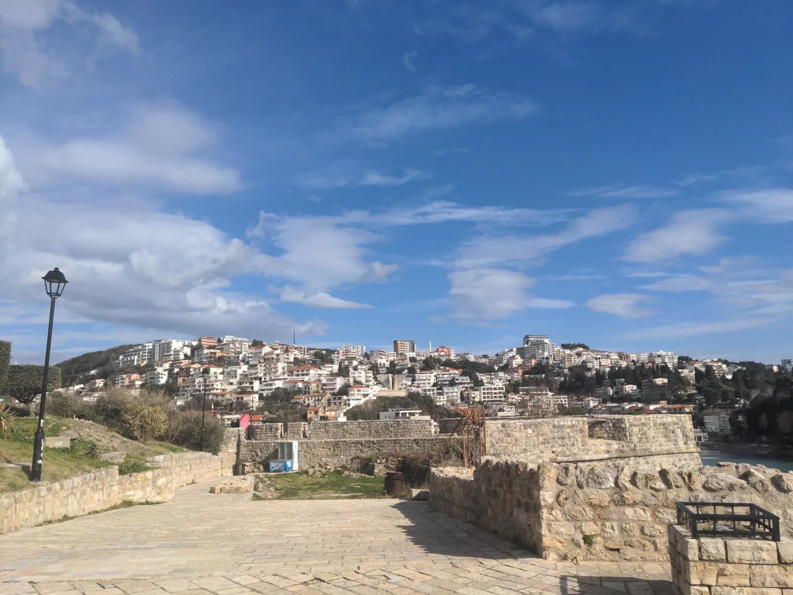 The view east from the walls of the Kalaja at Ulcinj: stone houses and terraces of the fortified old town in the foreground, the modern town and its beaches curving away beyond, and hills along the coast in the distance.