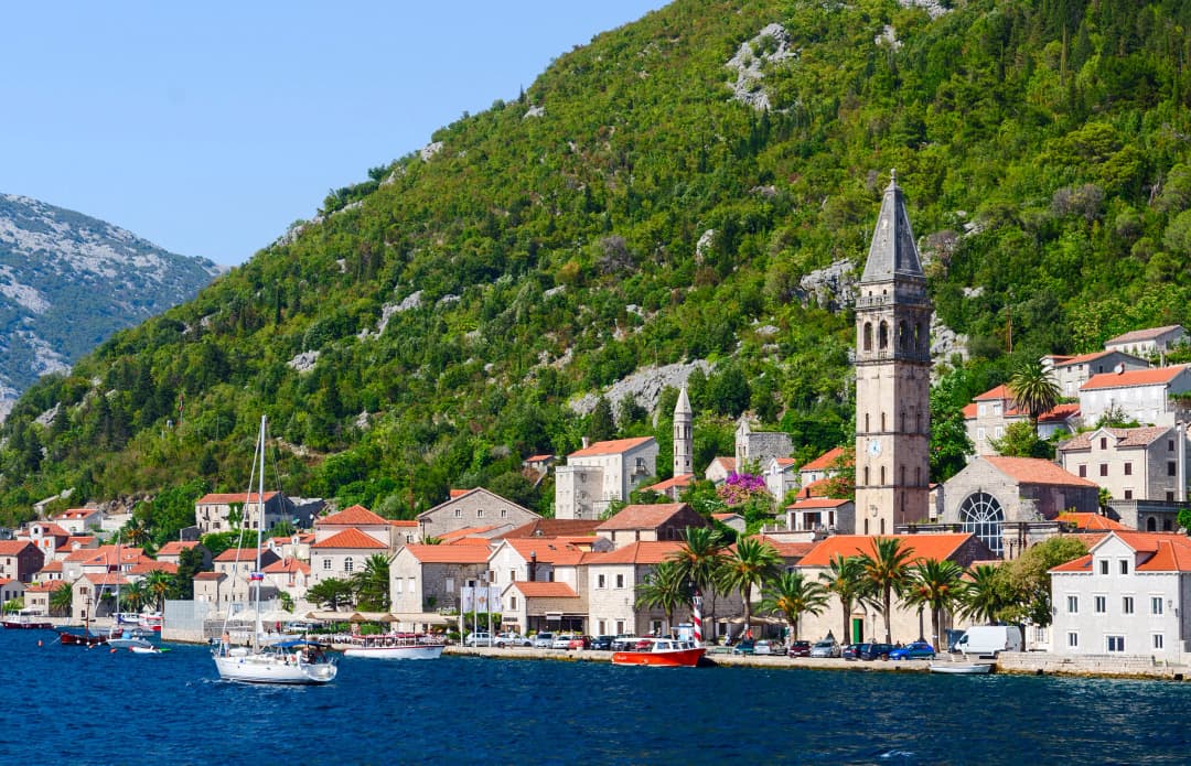 Perast hamn och klocktorn under ett brant berg