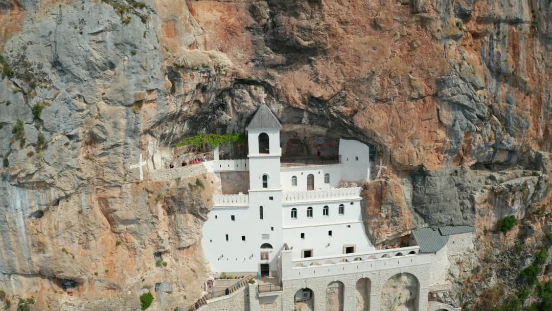 The monastery buildings set into the vertical rock face, with the Bjelopavlići plain opening out far below
