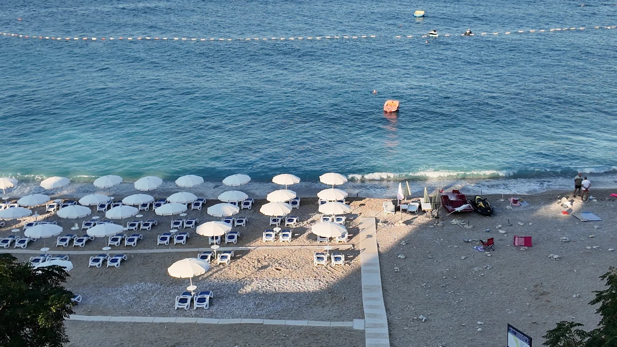 Veliki Pijesak from above: the arc of shingle, rows of parasols, the promenade and the islet Veliki Kamen just offshore