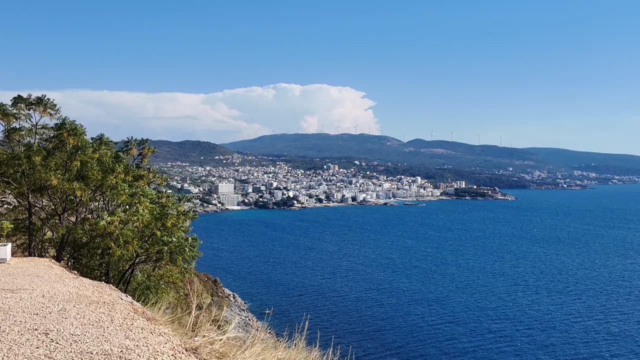 Veliki Pijesak from above: the arc of shingle, rows of parasols, the promenade and the islet Veliki Kamen just offshore