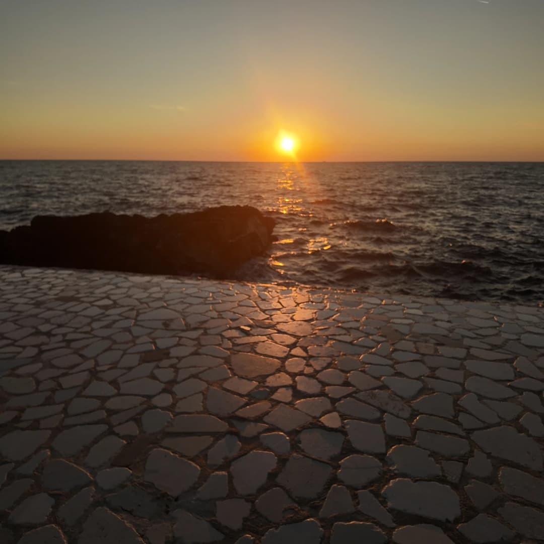 Sunce na horizontu nad mirnim morem, a njegova svjetlost teče preko nepravilno popločane kamene terase hotela za zalazak sunca