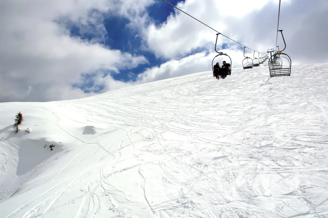A chairlift climbing over an empty groomed piste under a bright sky.