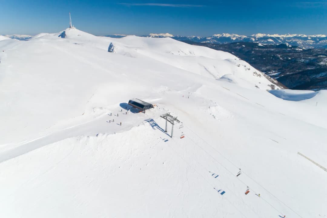 Aerial view of a ski area showing groomed pistes, lift lines and base buildings in the snow.