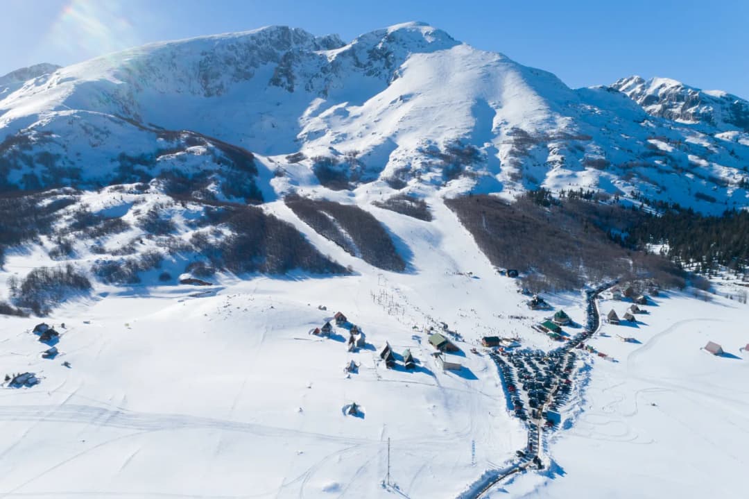 A snow-covered mountain massif rising steeply behind a village on the valley floor.