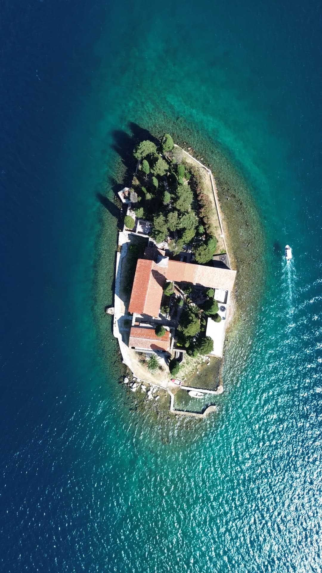 Utsiden av et restaurert barokk-palais-hotell i Perast i skumringen, med varmt lys som strømmer fra vinduene og bukten synlig bak