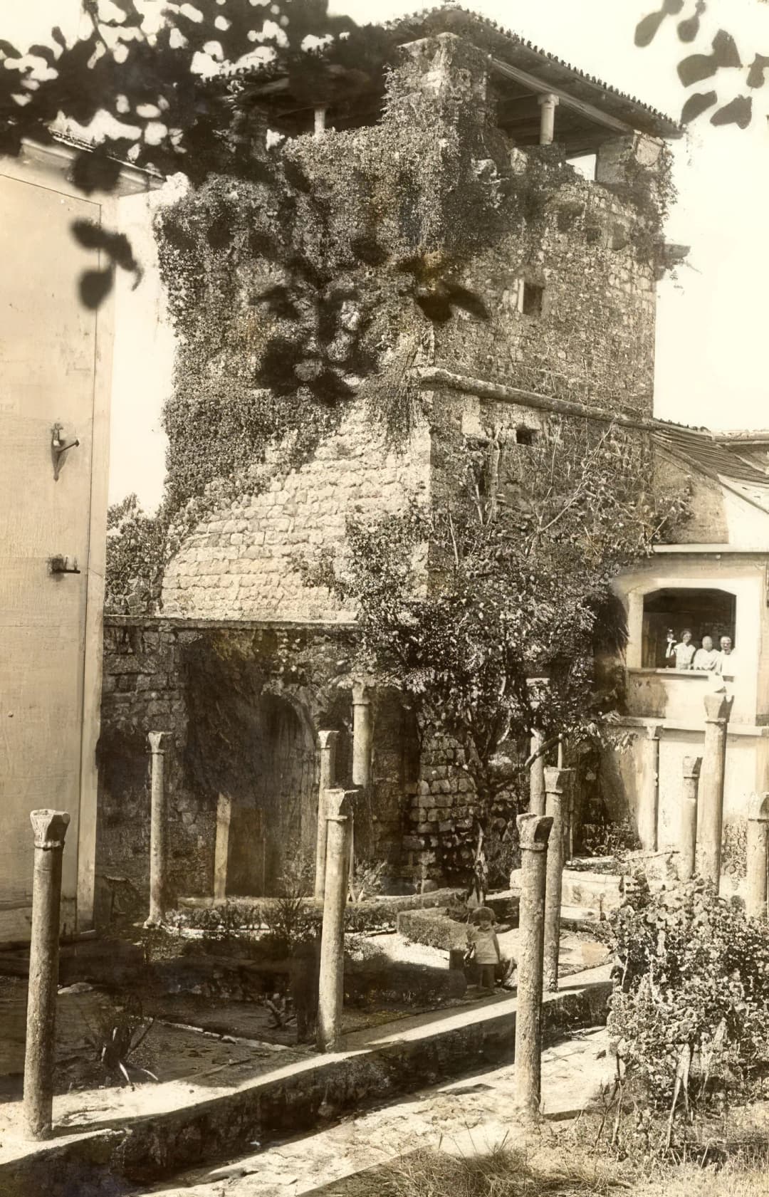 Archival photograph of the ivy-covered Buća-Luković tower with garden columns and residents on the loggia
