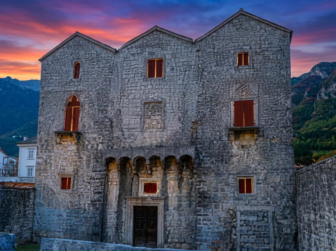 The roofless stone shell of the Tre Sorelle palace on the Prčanj shore, its Gothic facade pierced by three tall pointed windows.
