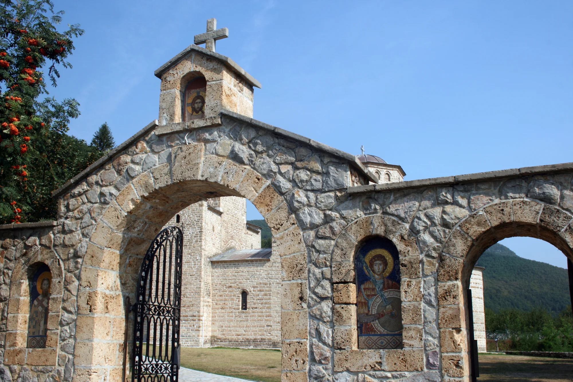 La portada de piedra del monasterio de Đurđevi Stupovi, con santos en mosaico en sus arcos y la iglesia al fondo