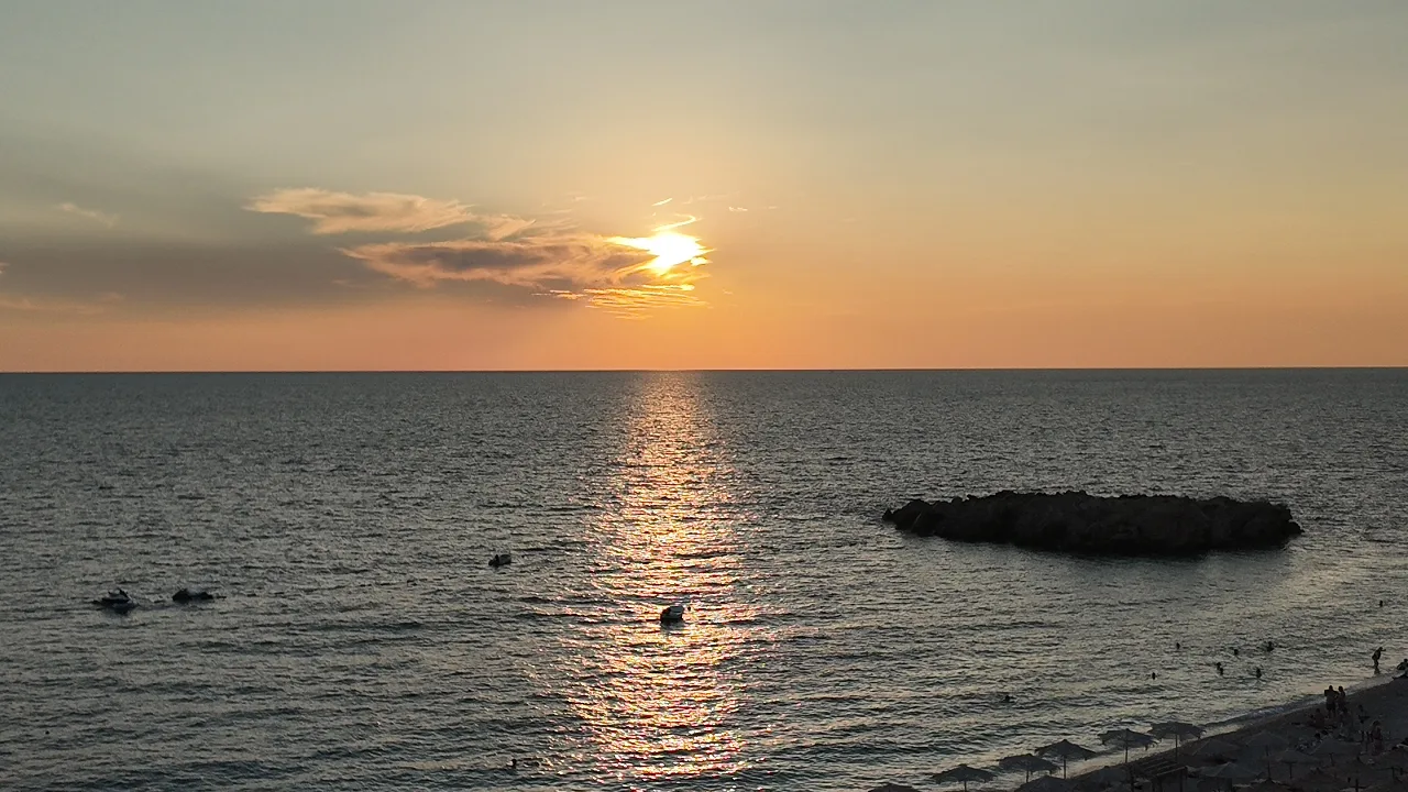 The sun behind a streak of cloud above the Adriatic, its path of light reaching the islet Veliki Kamen off Veliki Pijesak