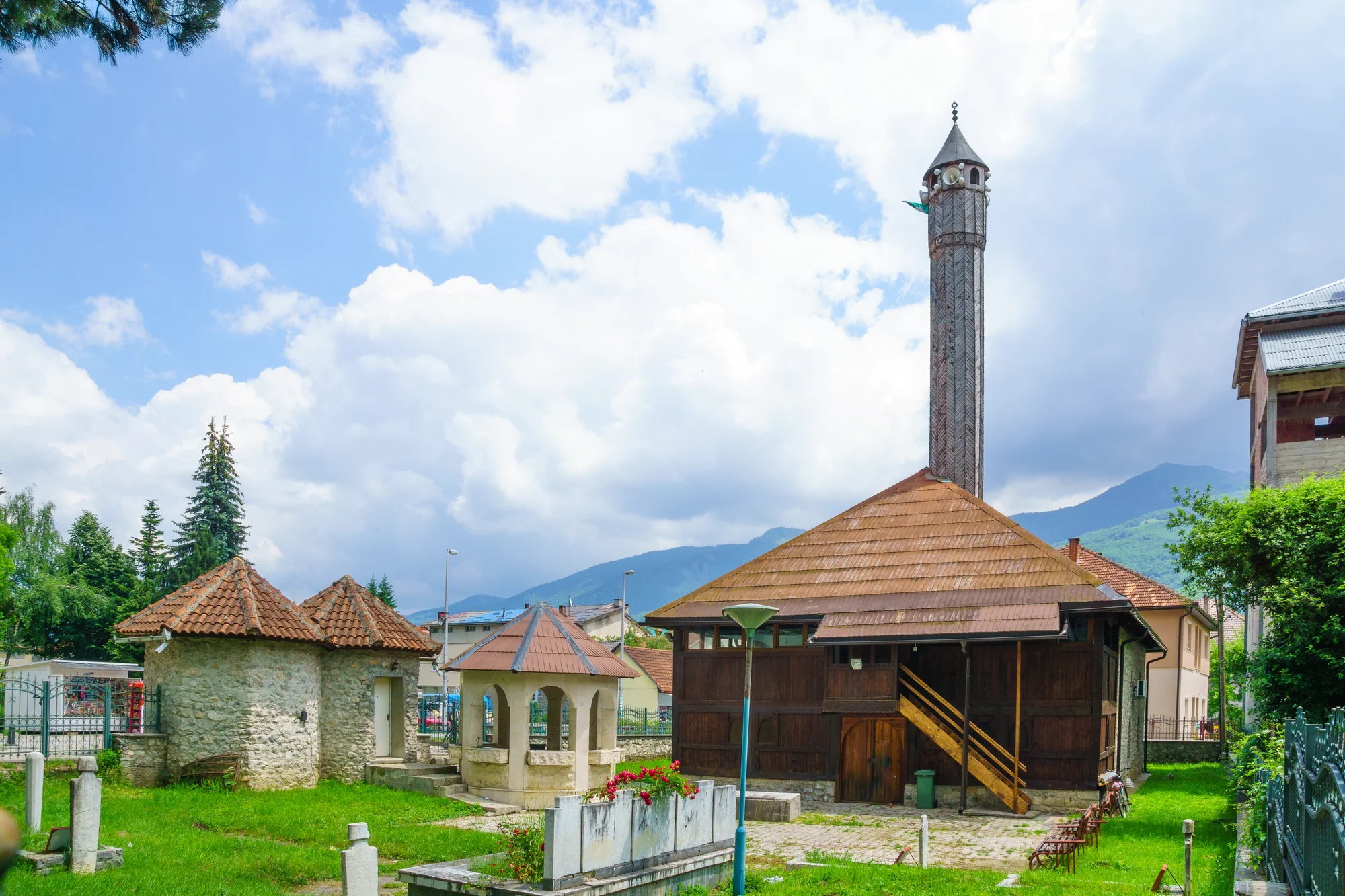 La vieja mezquita de fachada de madera de Gusinje: tejado piramidal de tablillas, un alto alminar de madera tallado en zigzag, un pozo de piedra con arcadas y una türbe de piedra en el cementerio