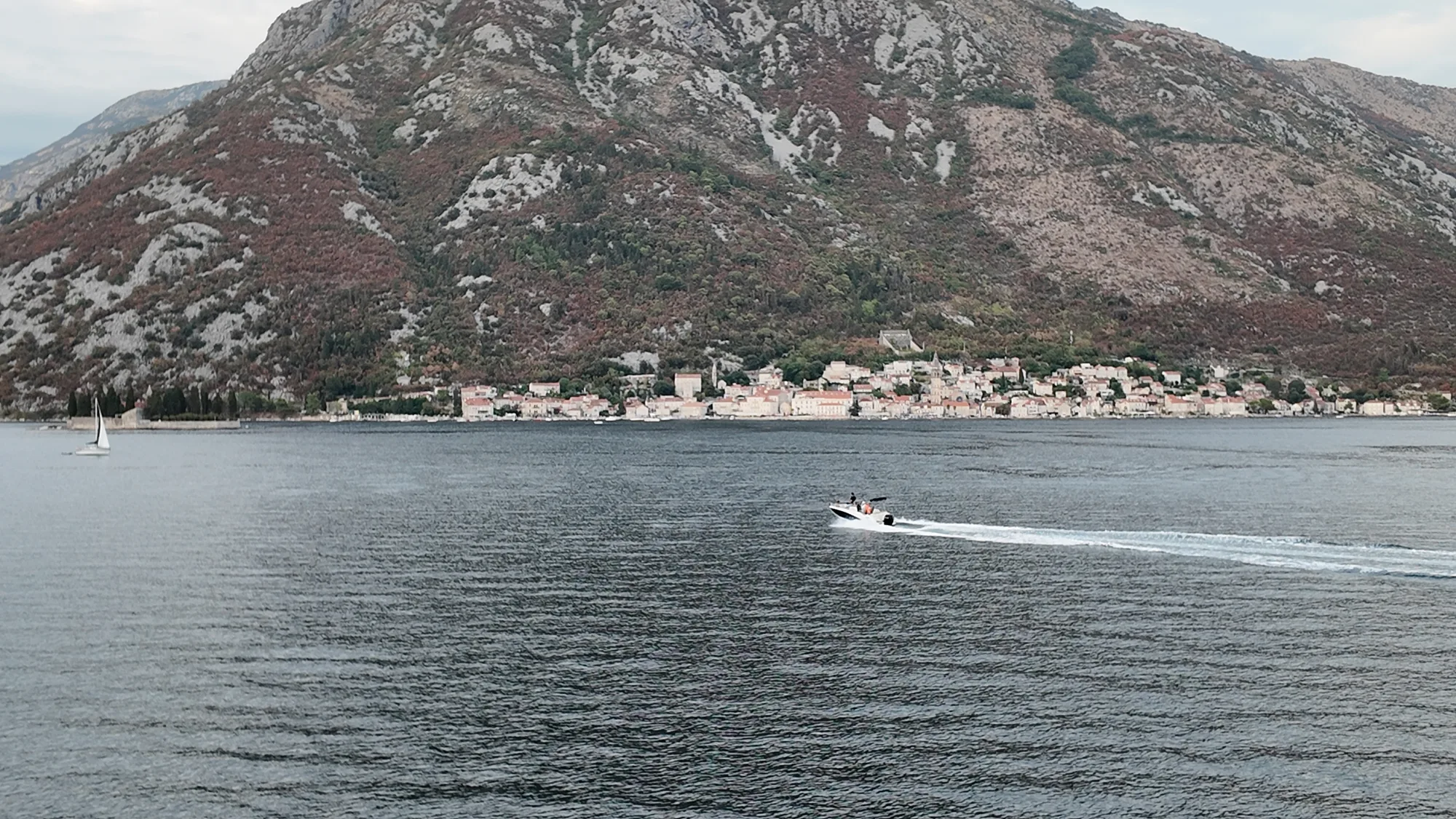 Perast strung along the foot of its mountain across the strait, a speedboat crossing