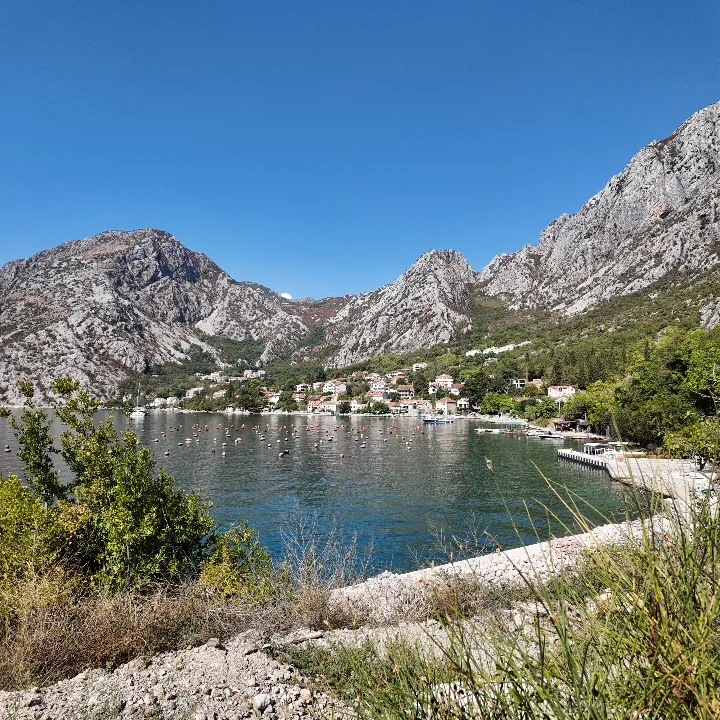 The houses of Orahovac strung along the shore beneath a bare limestone mountain, the inner Bay of Kotor still and blue in front of them