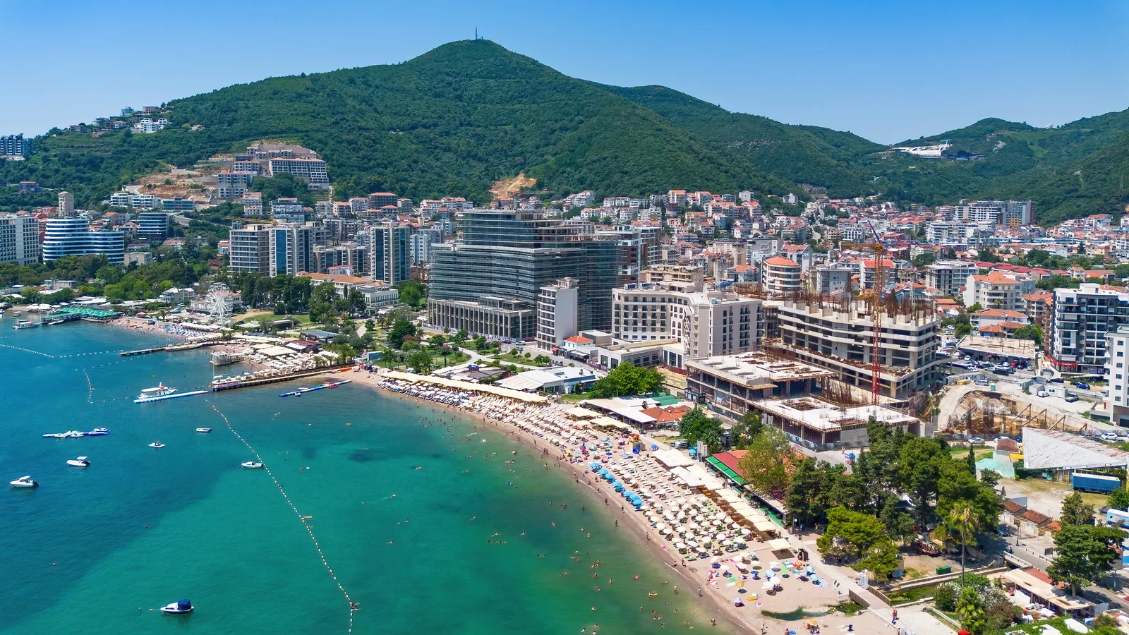 Luftaufnahme des Hauptstrands von Budva und der Wasserfronthotels unter der Altstadt, türkisfarbenes Adriatisches Wasser