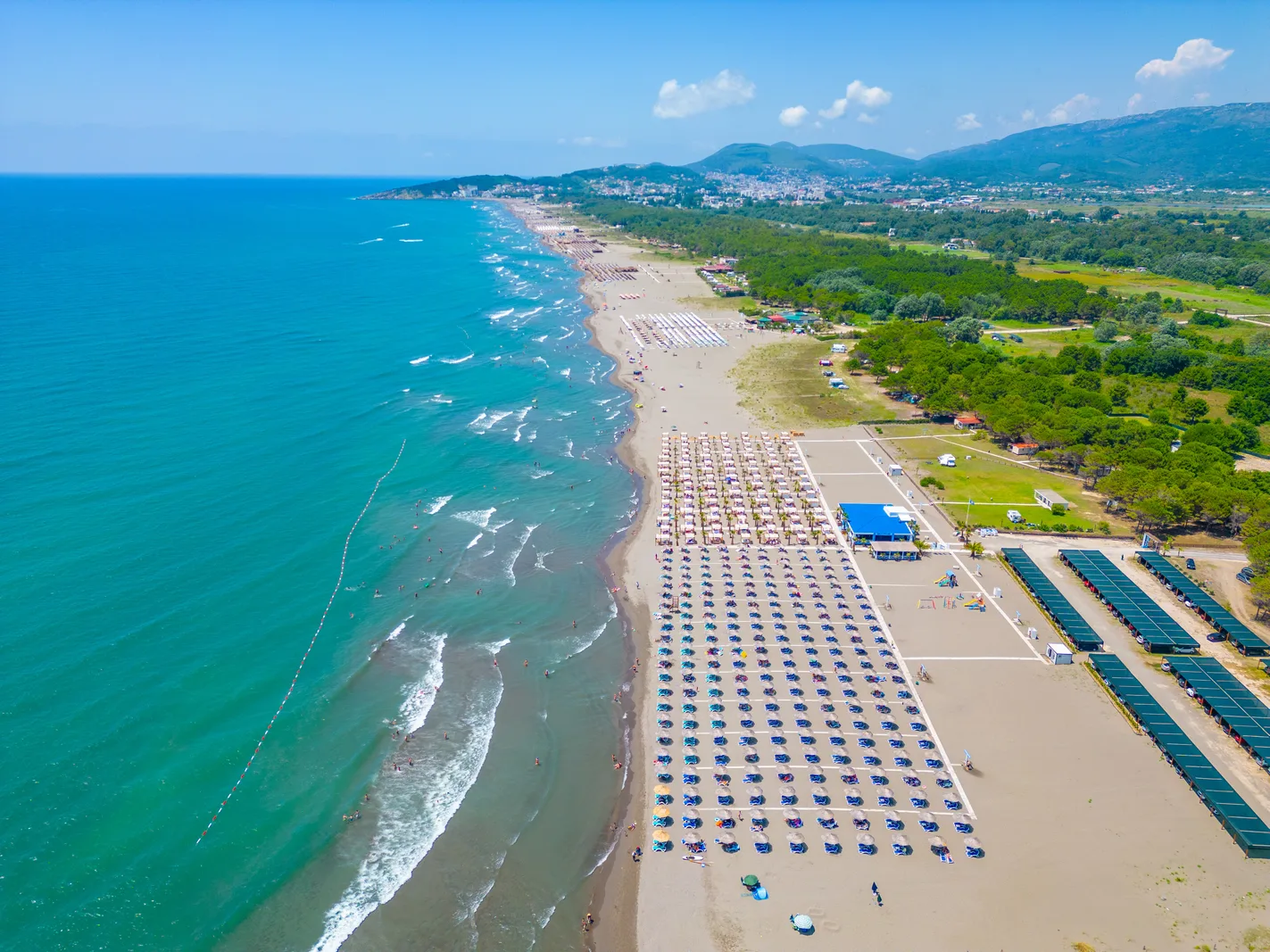Velika Plaža near Ulcinj: rows of sun loungers and parasols along a long sandy beach, with pine woods behind and hills in the distance