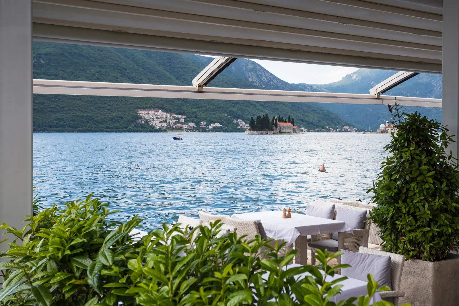 Paseo marítimo de Perast con campanarios barrocos y barcos dirigiéndose a la iglesia de la isla
